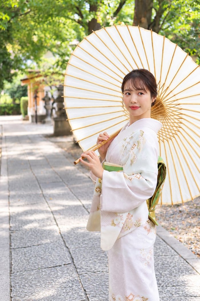 新しく入荷した淡い色合いの訪問着を着て和傘を持つ女性