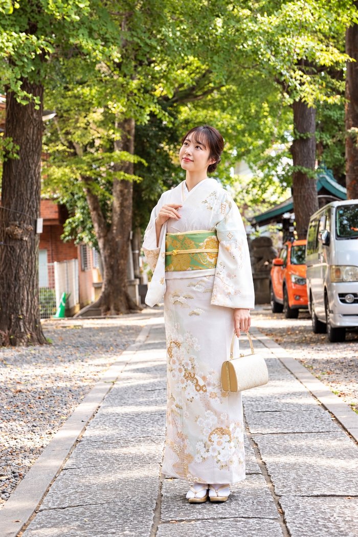 新しく入荷した訪問着を着て並木道に立つ女性